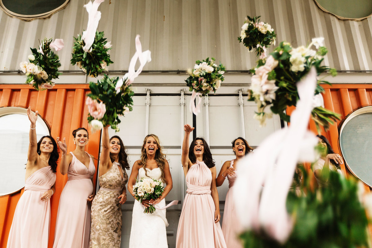 Bridesmaids throwing their bouquets at camera and laughing