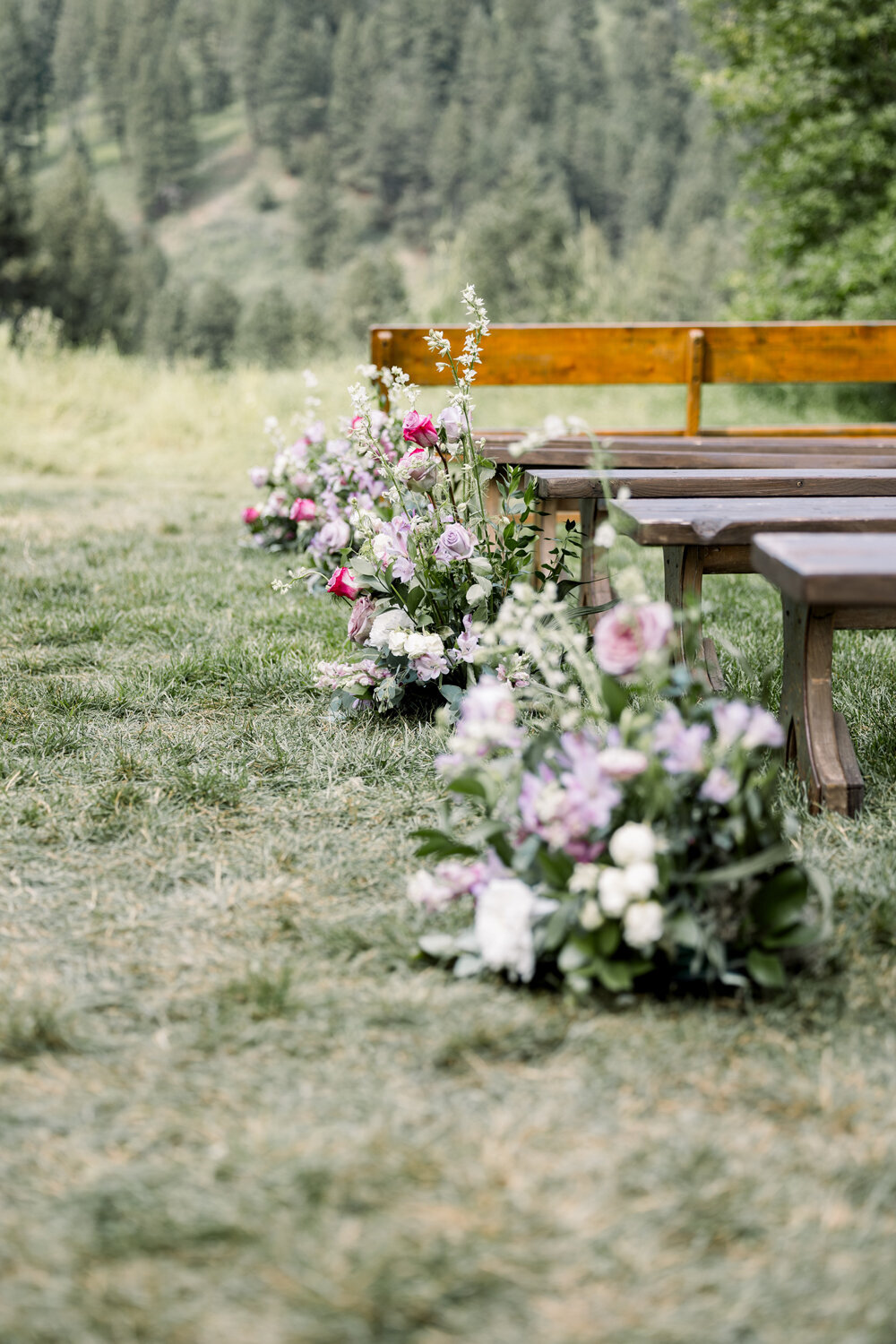 Floral arrangements in shades of purple and blush lining the aisle for a Montana summer wedding at The Woodlands at Cottonwood Canyon.