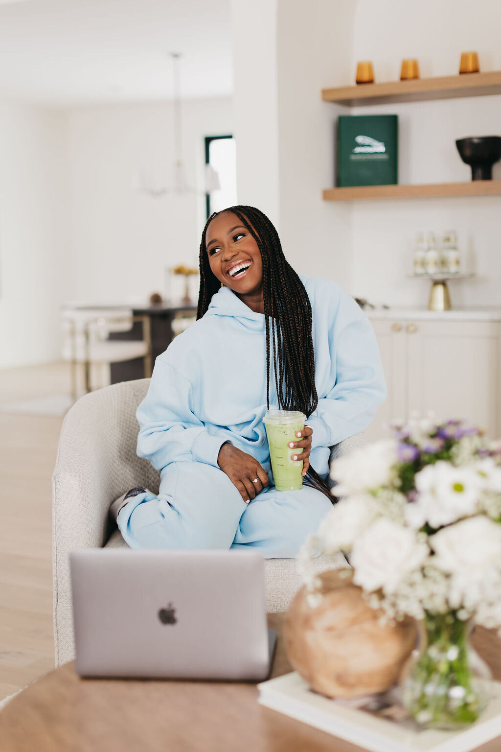 Juma Waganda in a blue sweatsuit sitting in a chair holding a matcha with her laptop on the table in front of her