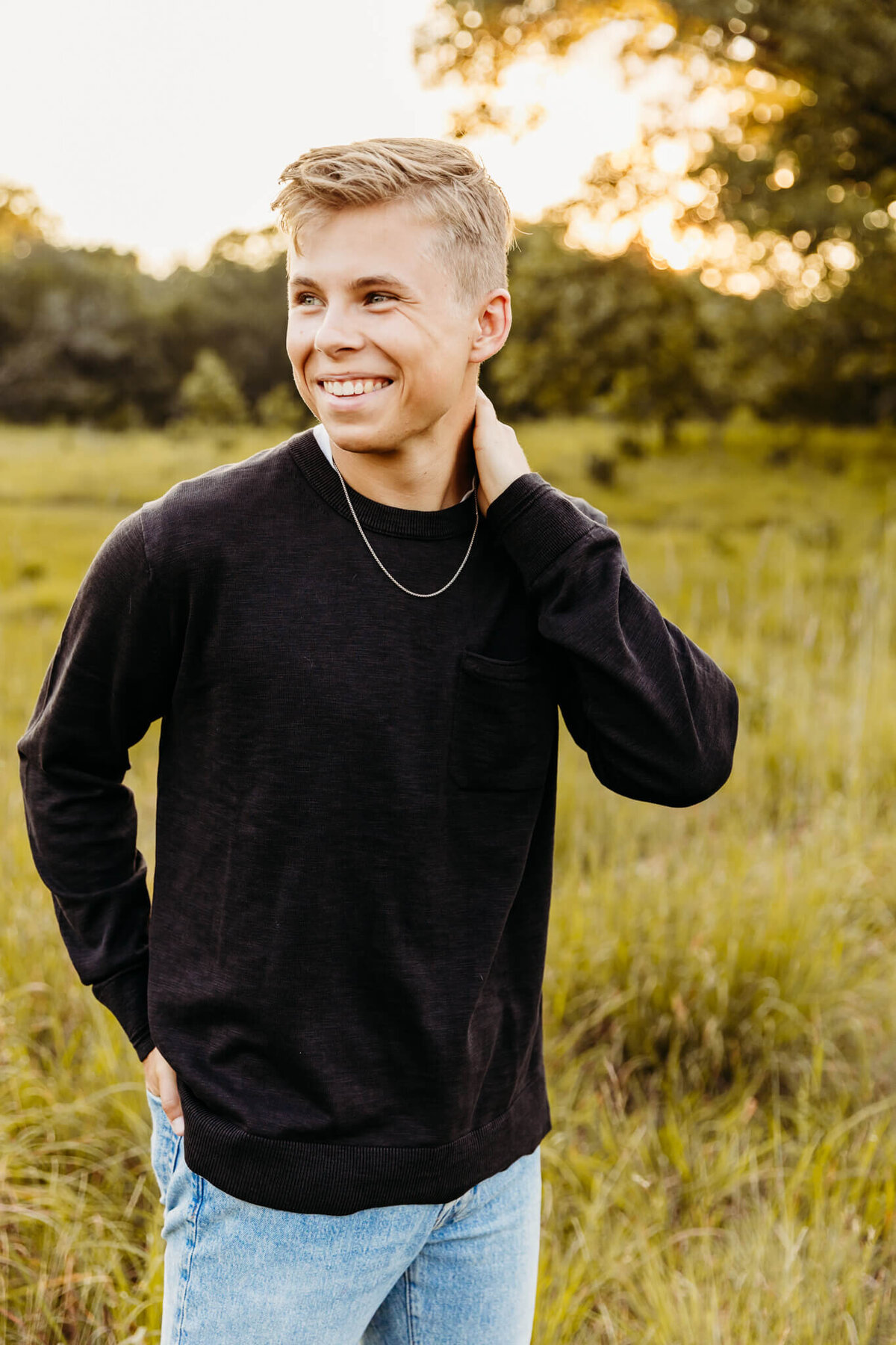 Teen boy rubbing neck with hand and laughing in a field