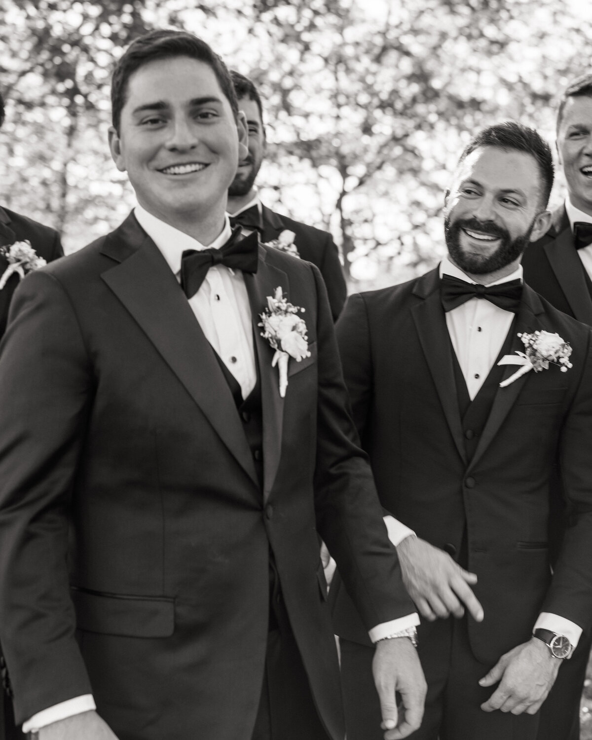 Groom shares a laugh with groomsmen in black tuxes, candid group shot by Philadelphia wedding photographer.