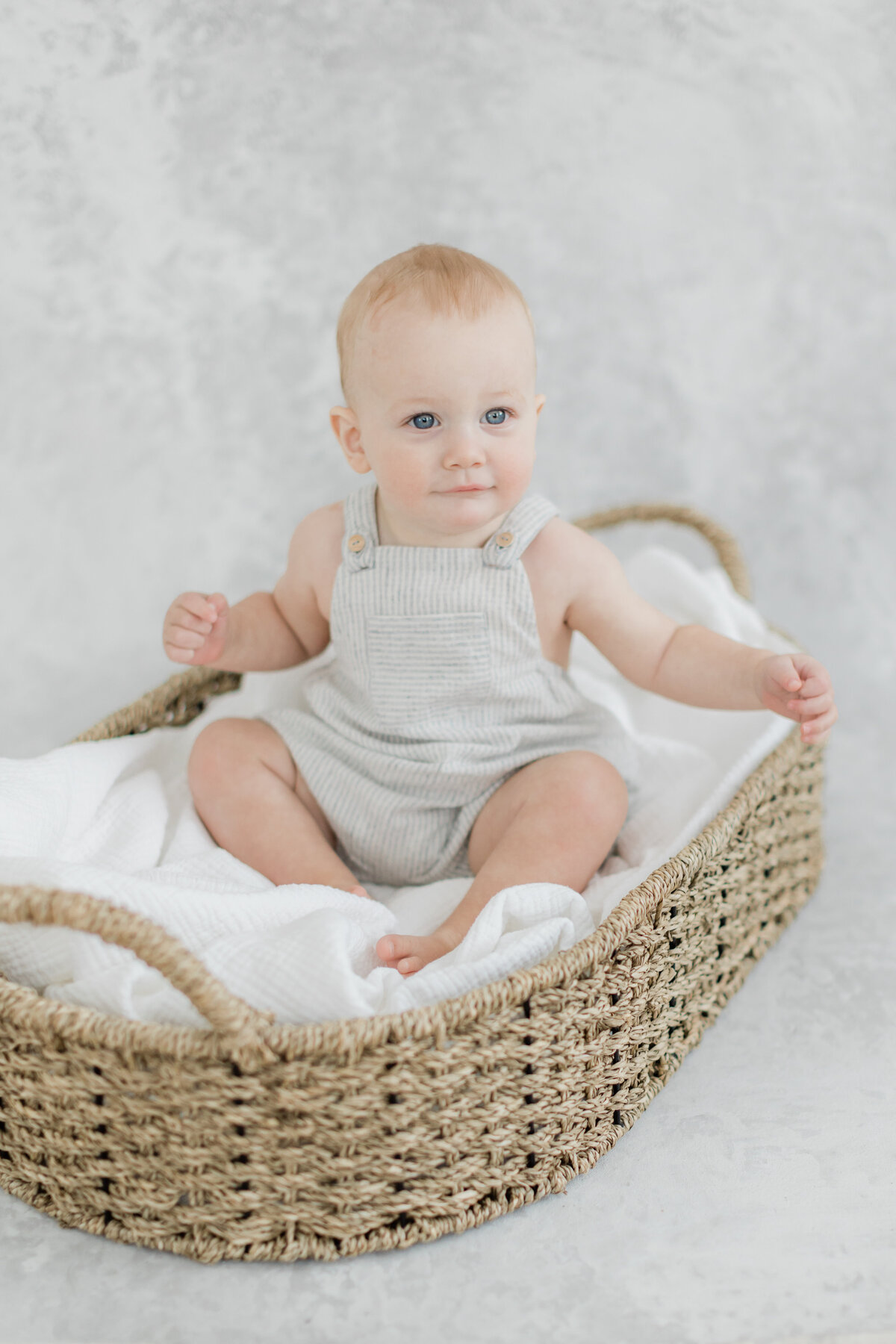 9 month old baby boy sitting in a Moses basket in front of a hand painted backdrop in Philadelphia Portrait Photographer Tara Federico's Haddonfield NJ studio