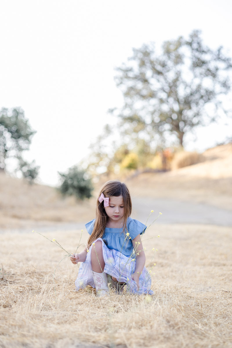 Young girl sitting on the ground and exploring wildflowers during an outdoor photoshoot in San Jose