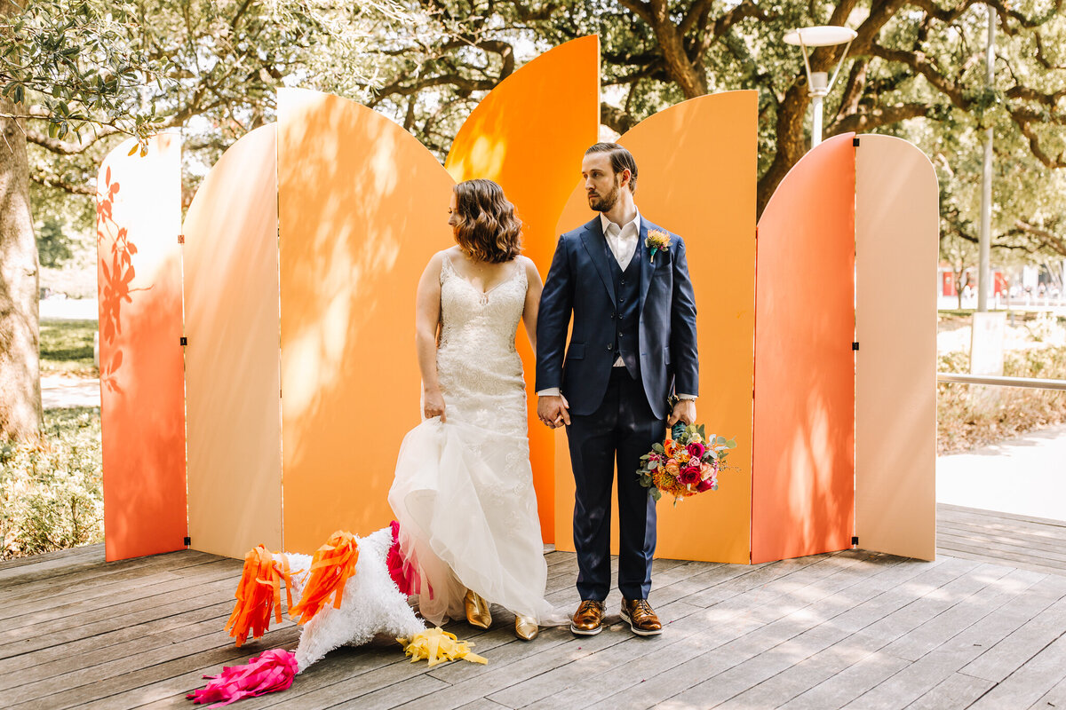 Bride and groom standing in front of a large orange colored arches backdrop