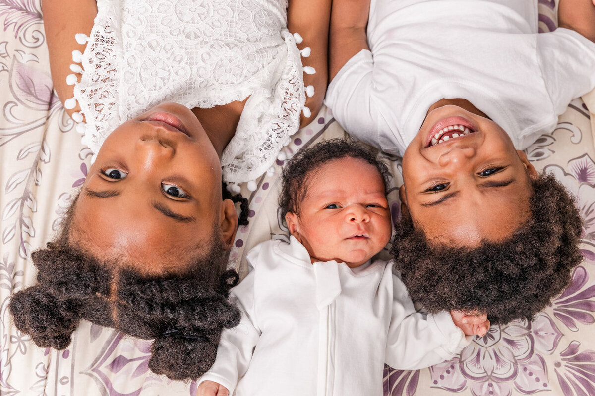 siblings todlers and newborn laying on a bed picture taken from above Laure Photography Atlanta family and newborn photographer