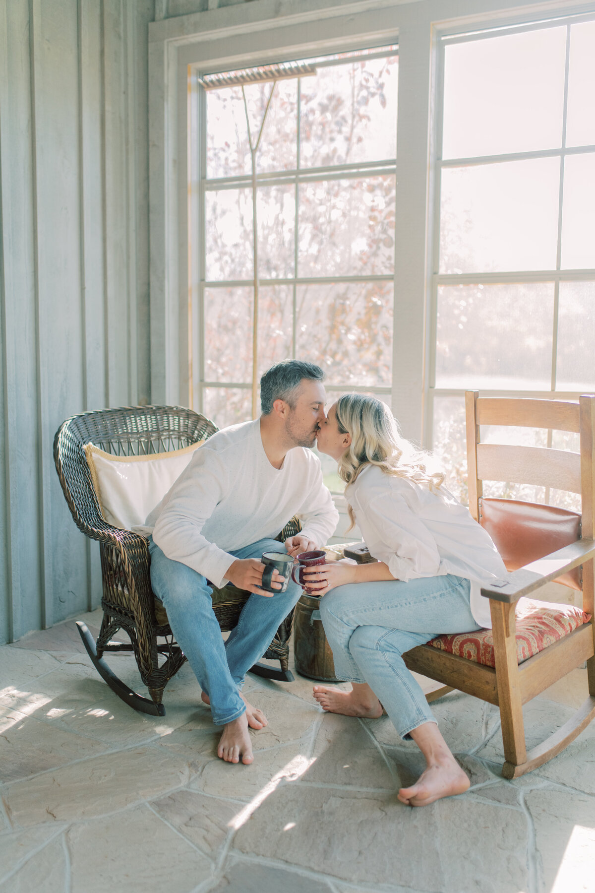 A tender kiss shared in the warm glow of a sunlit room at Elora Mill, with golden light filtering through the window.
