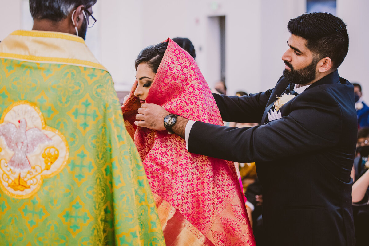 Indian christian malayali groom putting the manthrakodi sari over the bride's head during the ceremony