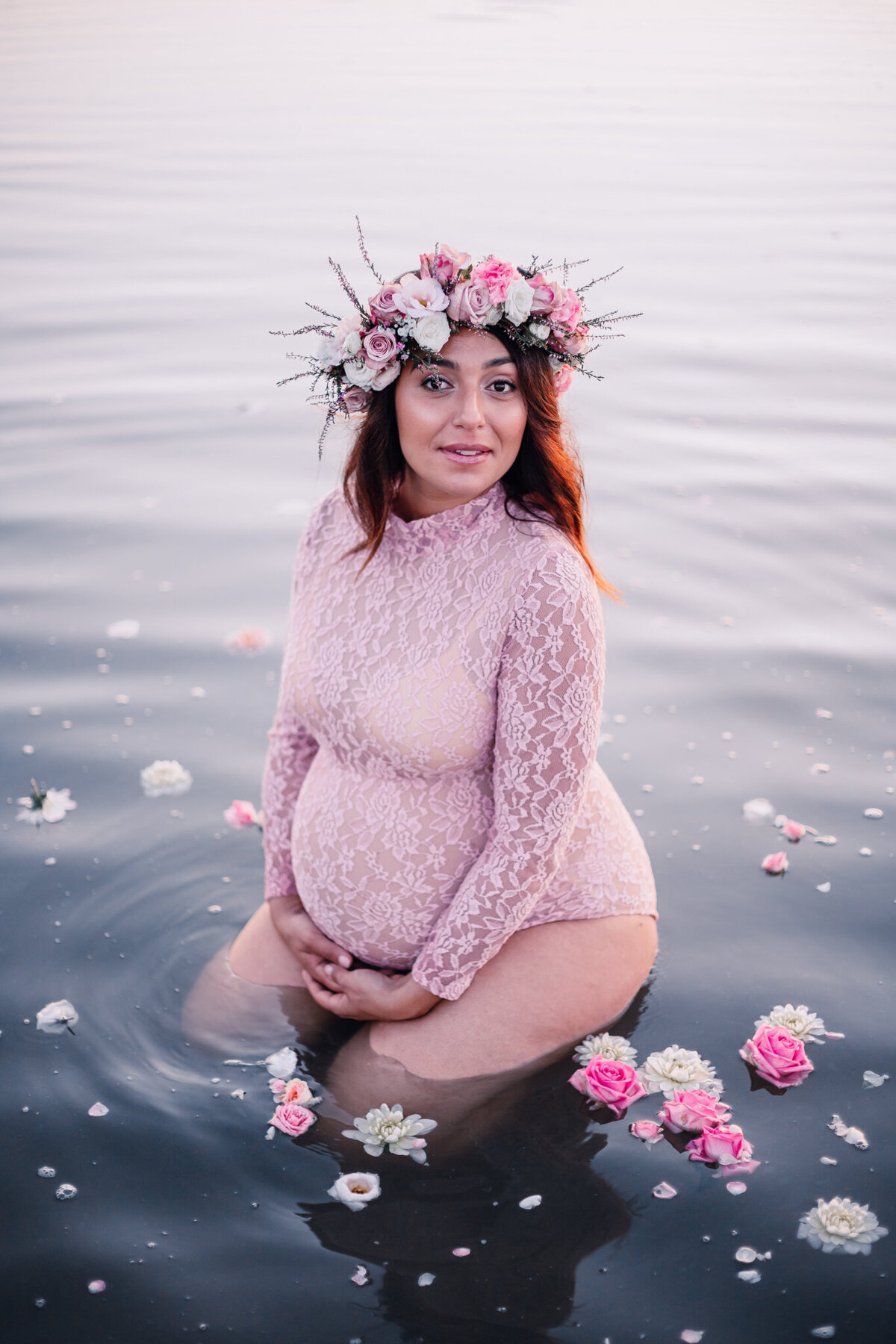 en gravid mamma sitter i vattnet i en rosa body med blommor i vattnet