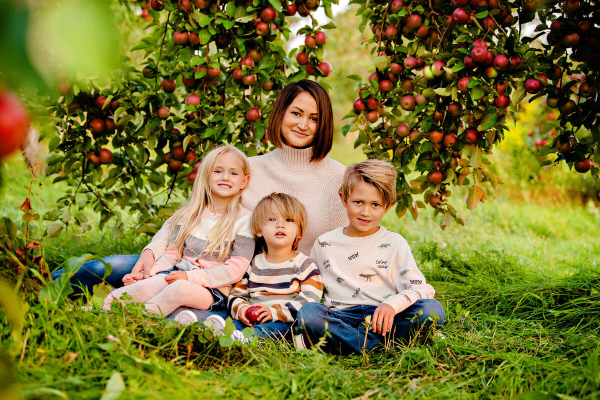 Mom sitting under and apple orchard tree for her fall family photos in Burlington, ON
