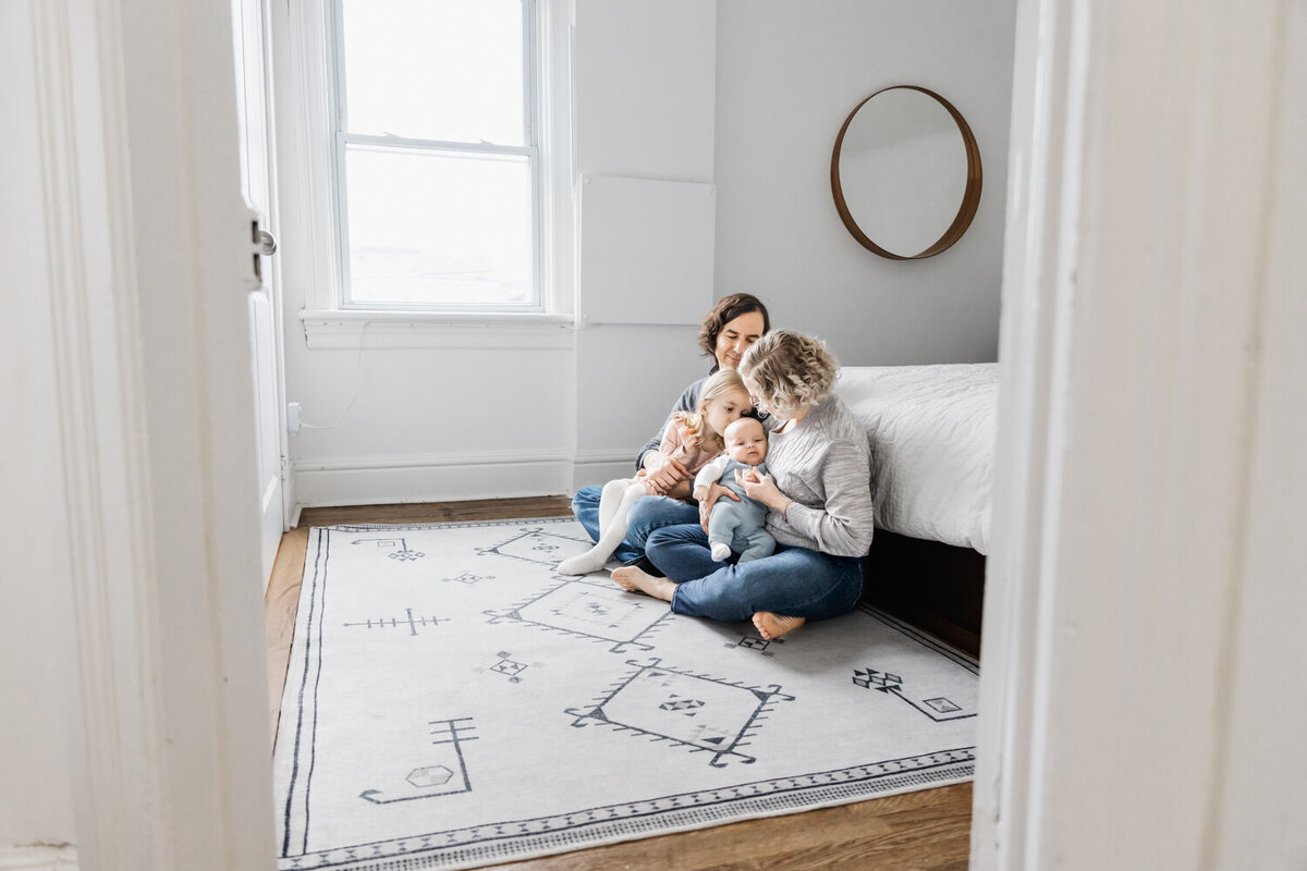 Family of 4 sitting on cream rug in main bedroom during Toronto Newborn Photography session