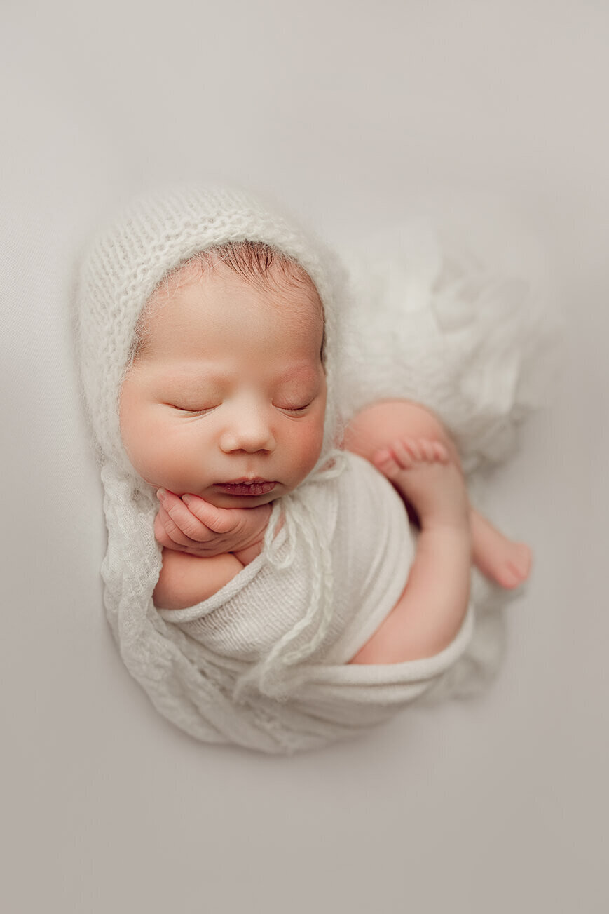 Sleeping newborn girl holding chin wrapped up