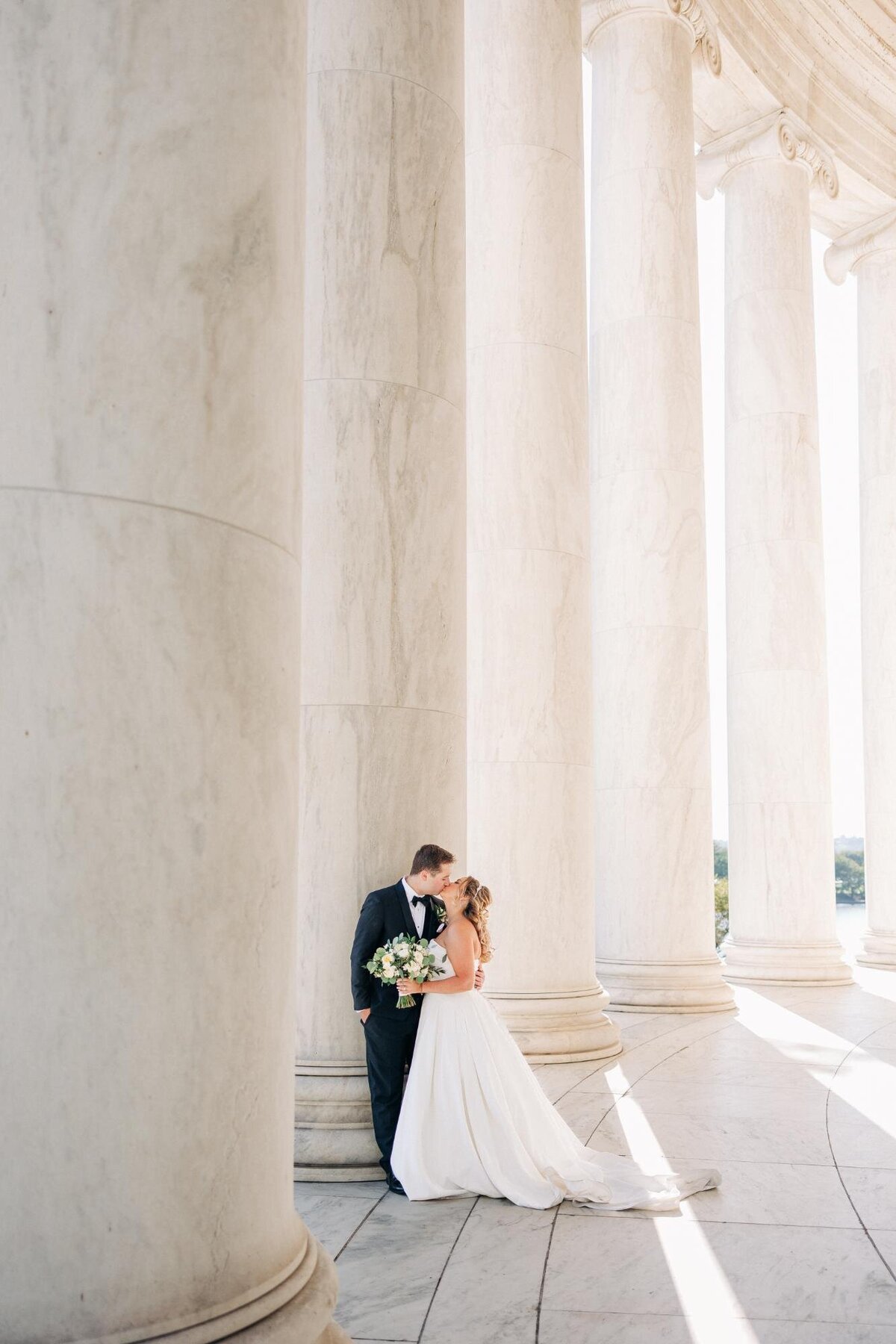 A couple in wedding attire sharing a moment among classical columns.