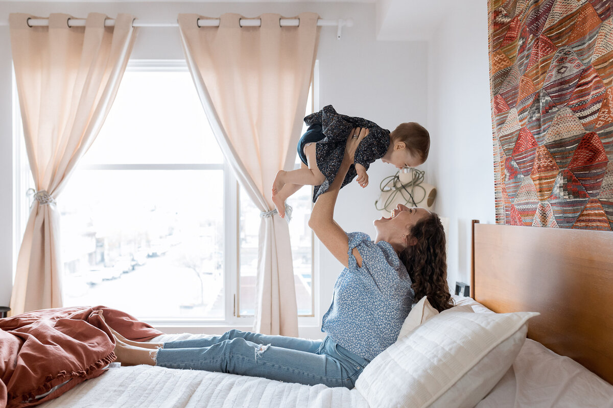 Family Photographer, A mother joyfully lifts her child in the air on her bed