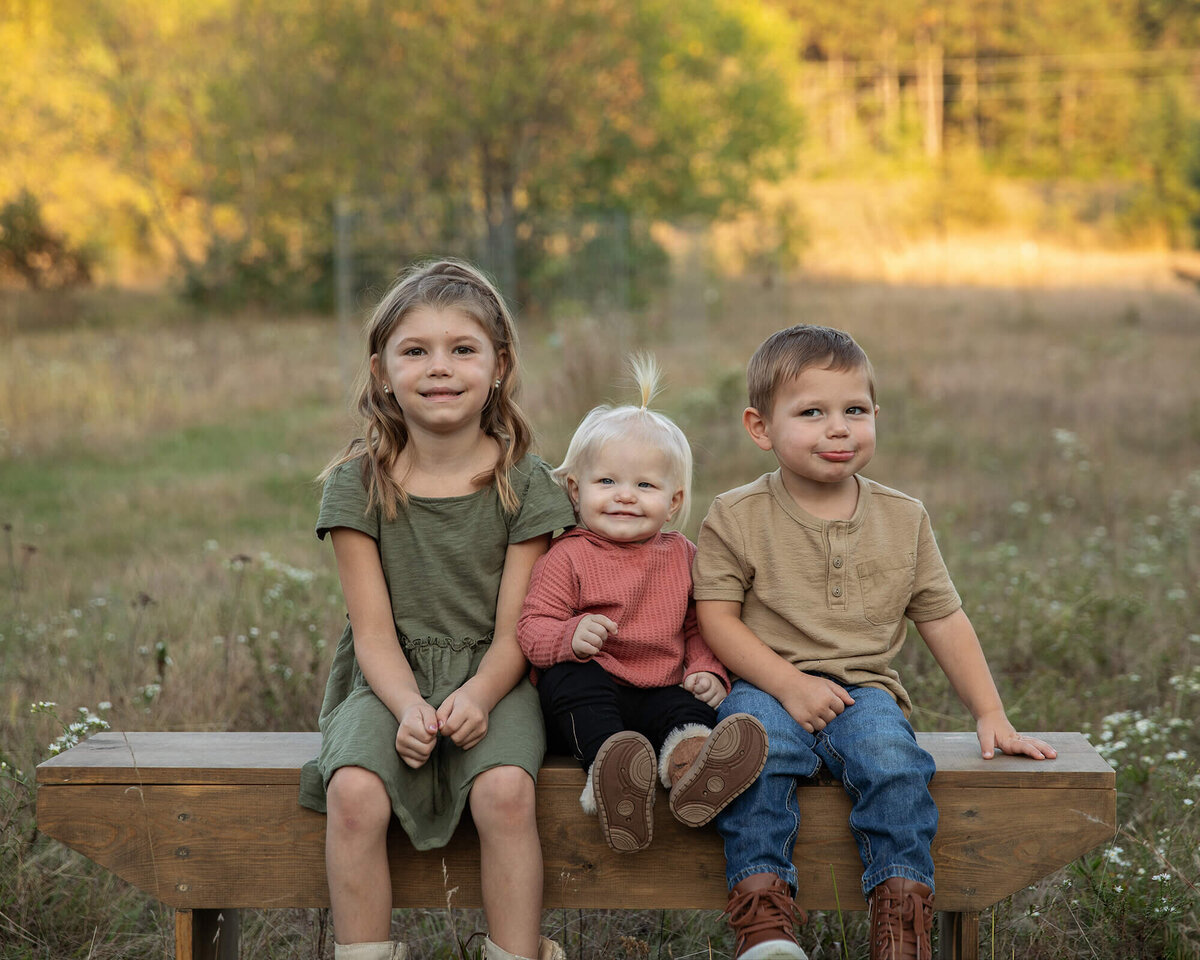 Two sisters and a brother sitting together on a bench on a fall evening.