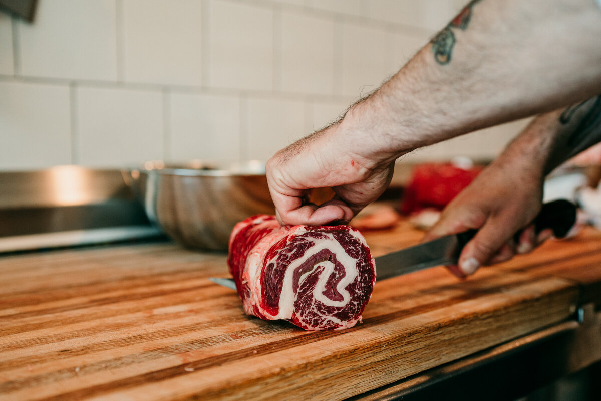close up of a marbled cut of meat and a butchers hand