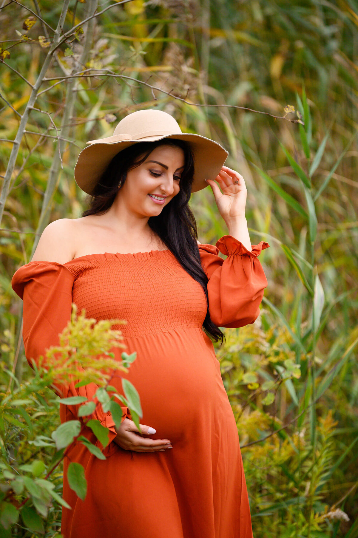up-close photo of pregnant woman wearing an orange maternity dress and beige hat for her outdoor fall maternity photos in Burlington
