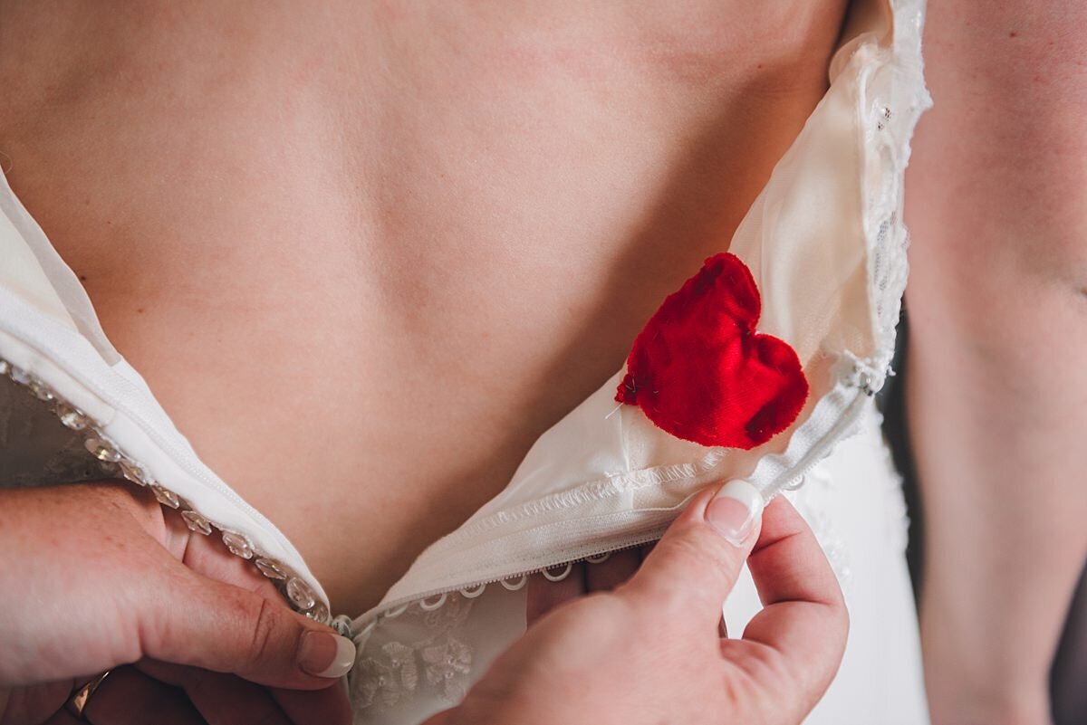 A small red heart sewn into the back of a wedding dress as the beaded bodice is buttoned up with tiny buttons.
