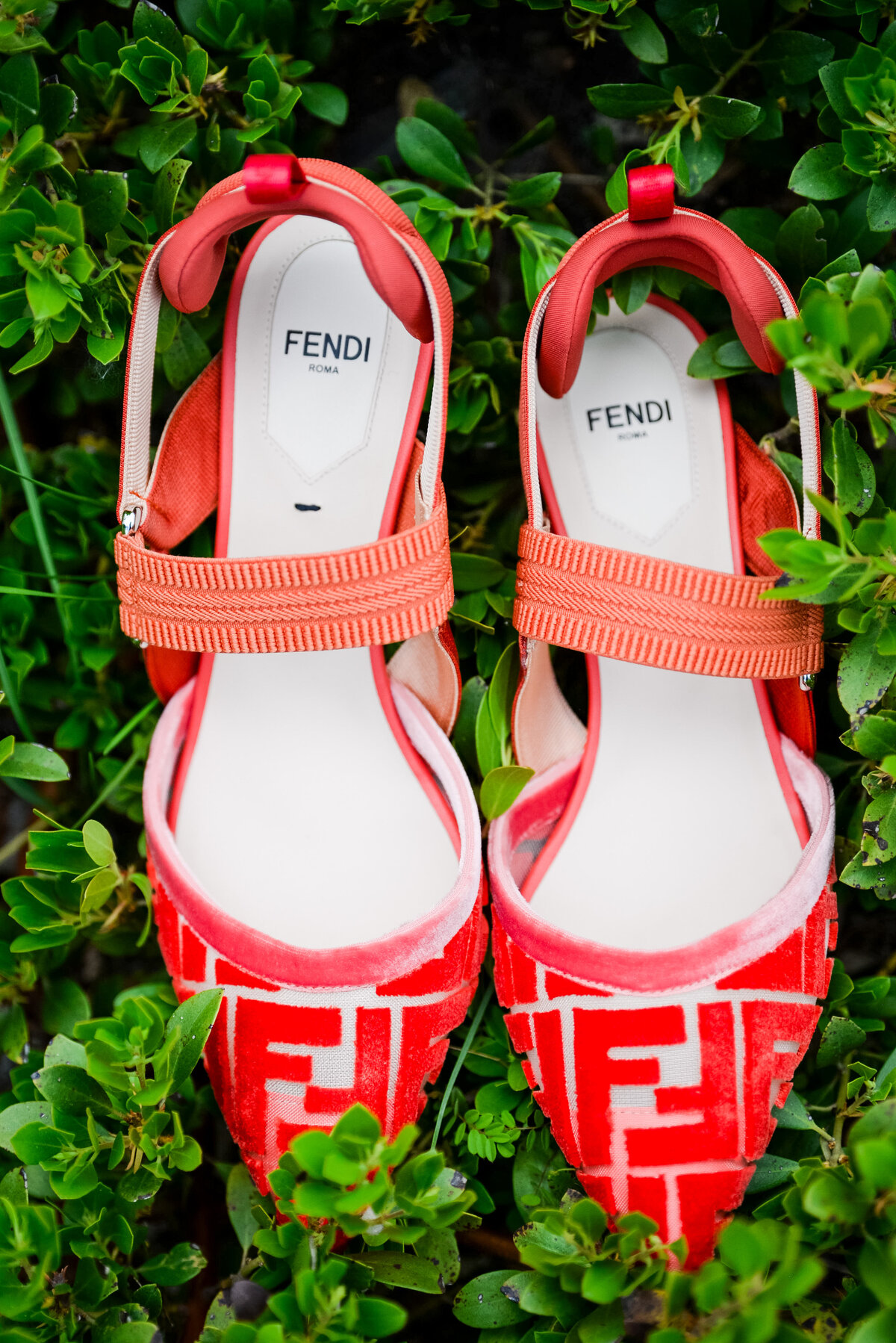 A pair of bright red Fendi heels sits in a patch of greenery.