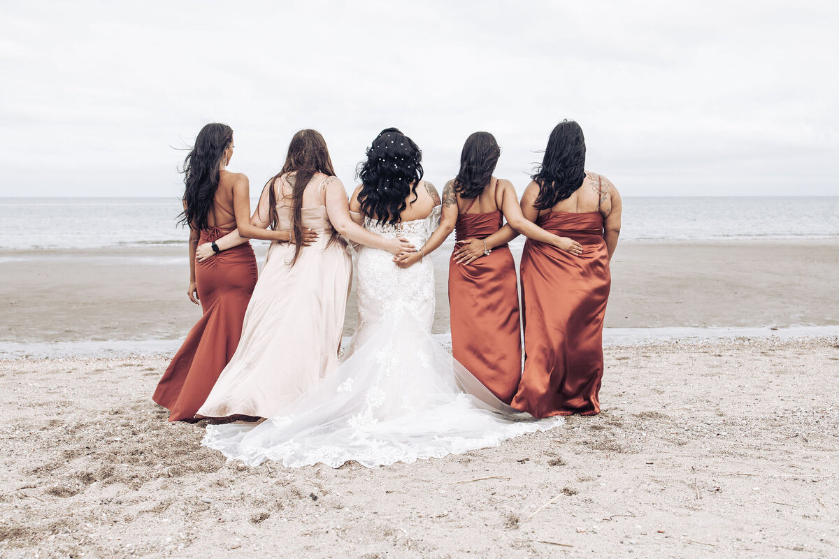 a bride linking arms with her bridesmaids on the beach