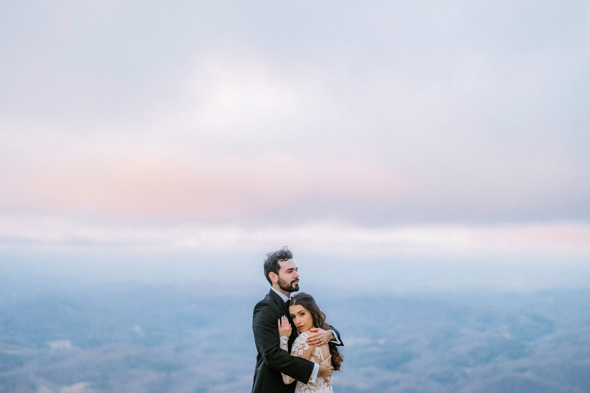 Bride and Groom embrace on a mountaintop at sunset