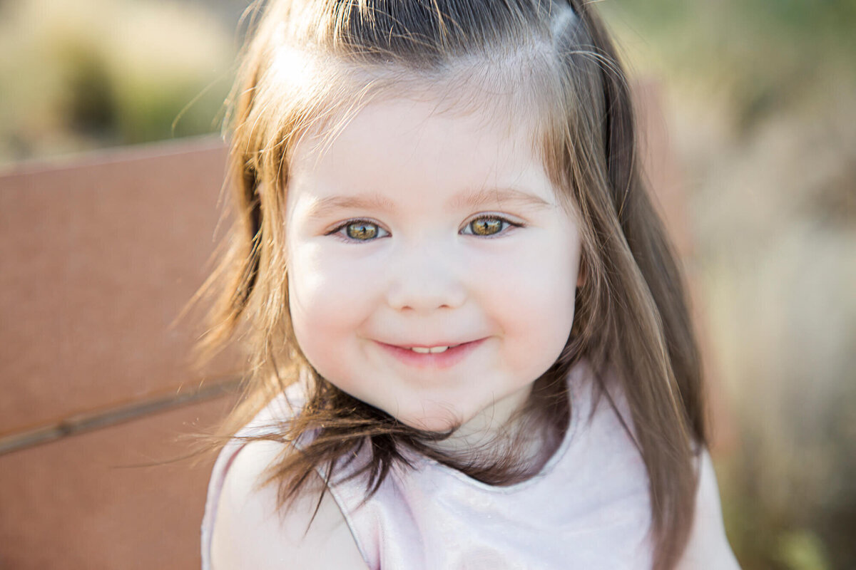 Happy brown haired toddler girl smiling on a park bench