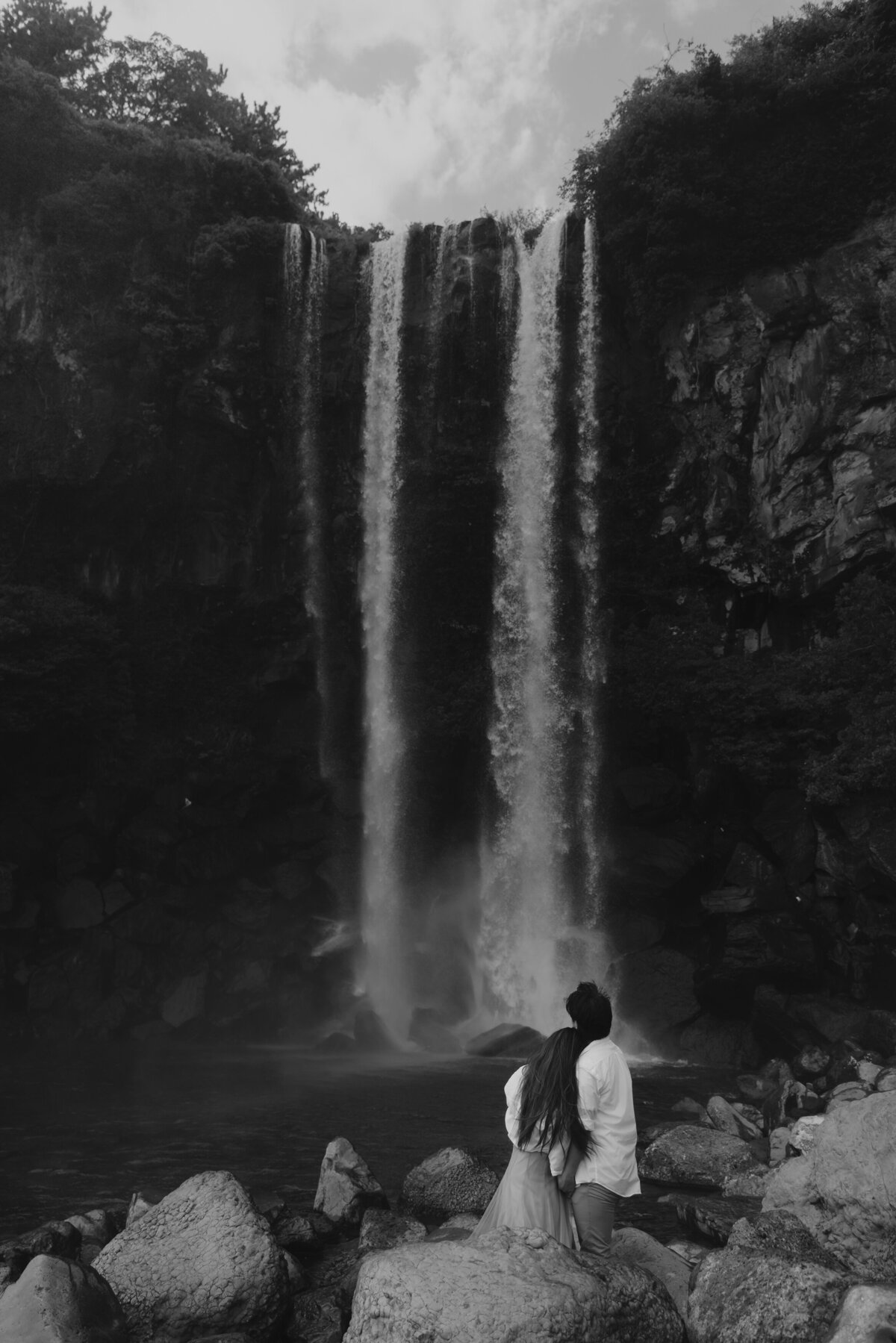 the bride leaning her head to the groom's shoulder while facing the waterfall in jeju island