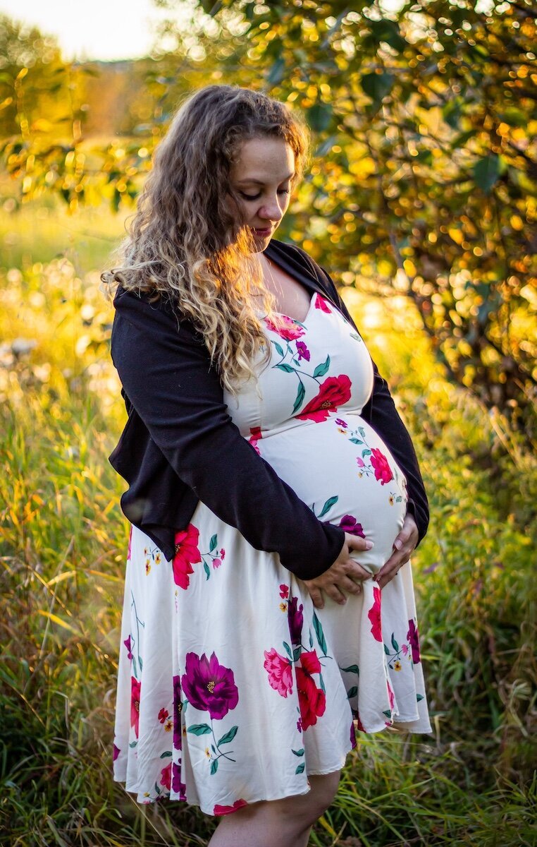 a pregnant woman wearing a white floral dress holding her belly