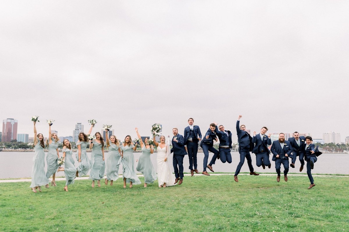 Bride and Groom jump for joy along with the bridal party with the ocean behind them