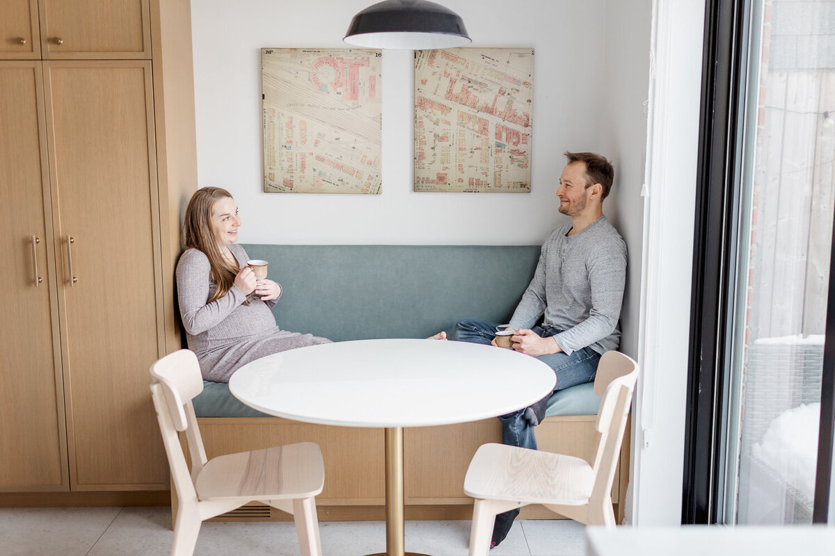 Pregnant redhead wearing brown dress sitting in kitchen with her husband enjoying a morning drink