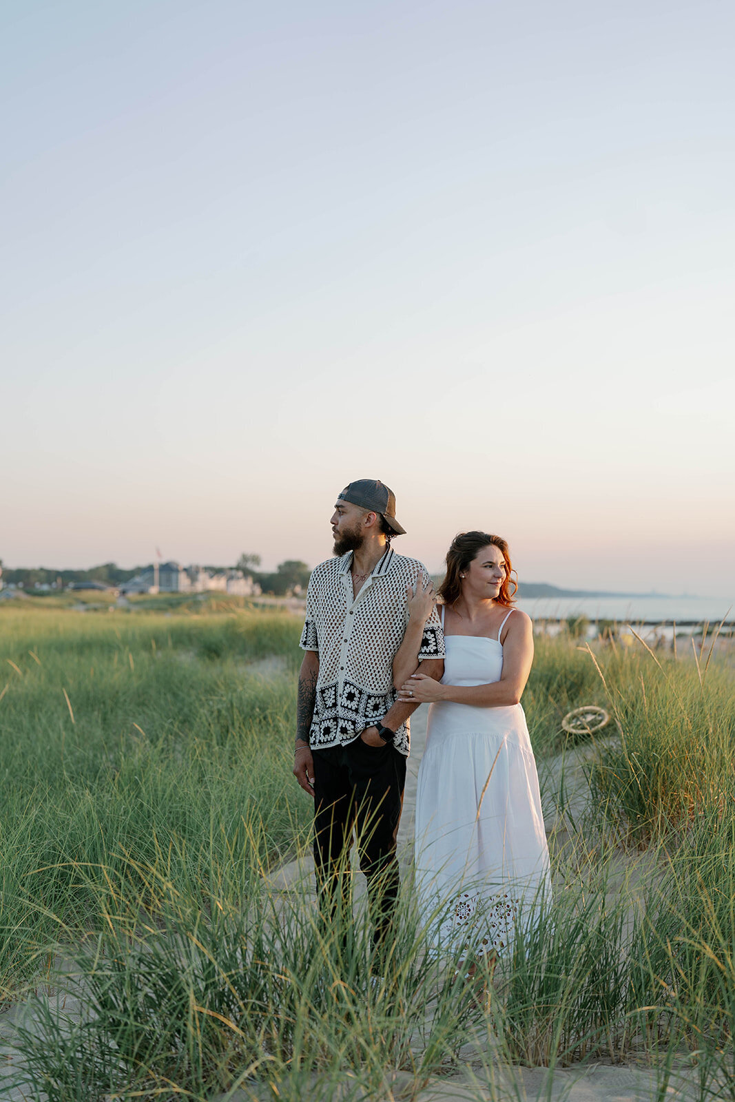 Engaged couple embracing in tall beach grass at New Buffalo, Michigan during golden hour