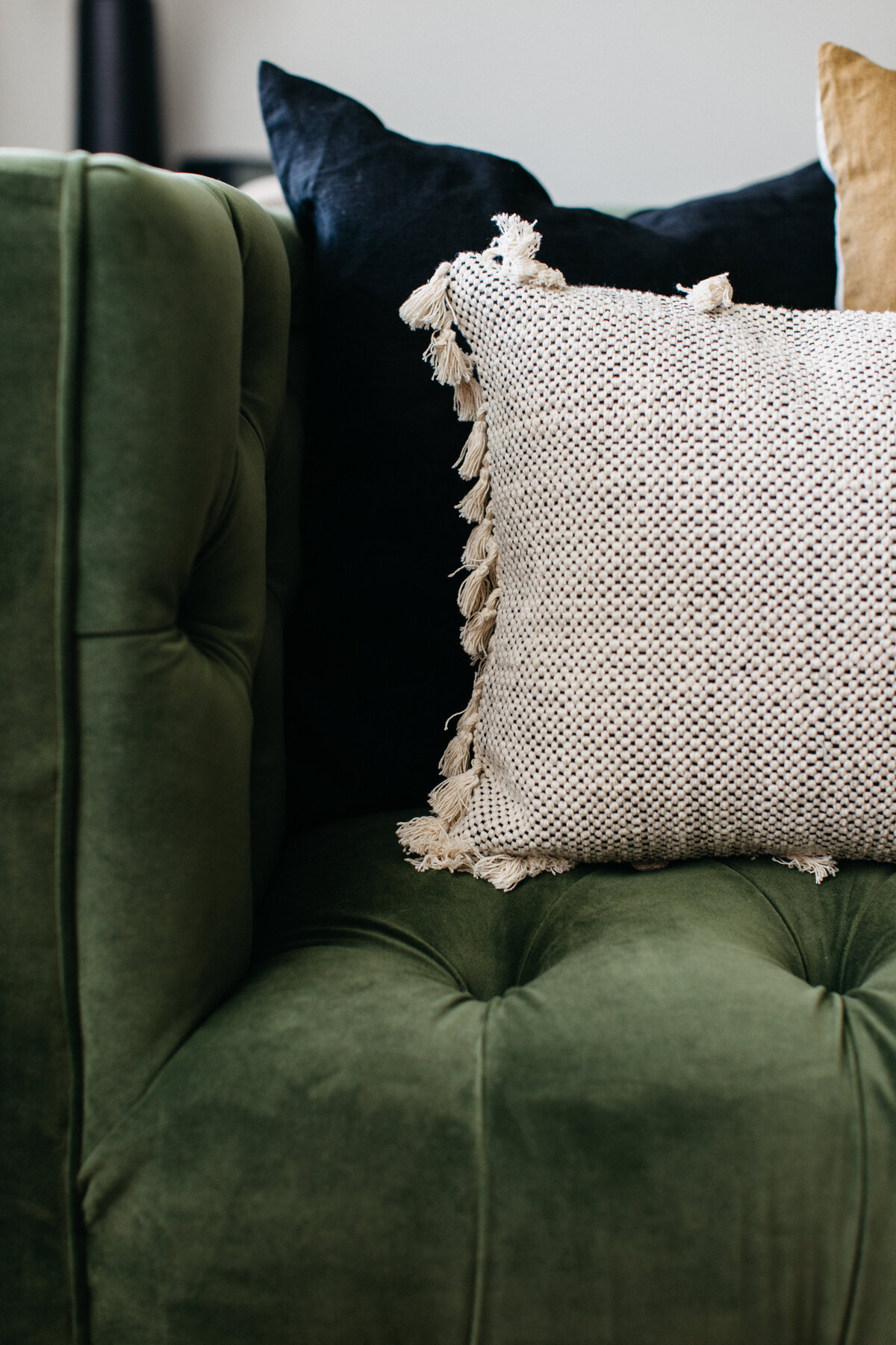Green velvet button tufted upholstered sofa with variety of neutral colored cottonthrow pillows