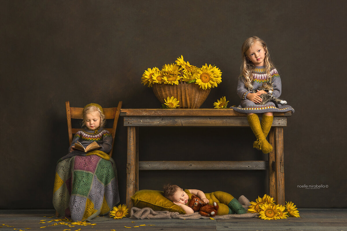 Children sitting at a wooden desk reading and playing. Baby sleeping under the table.