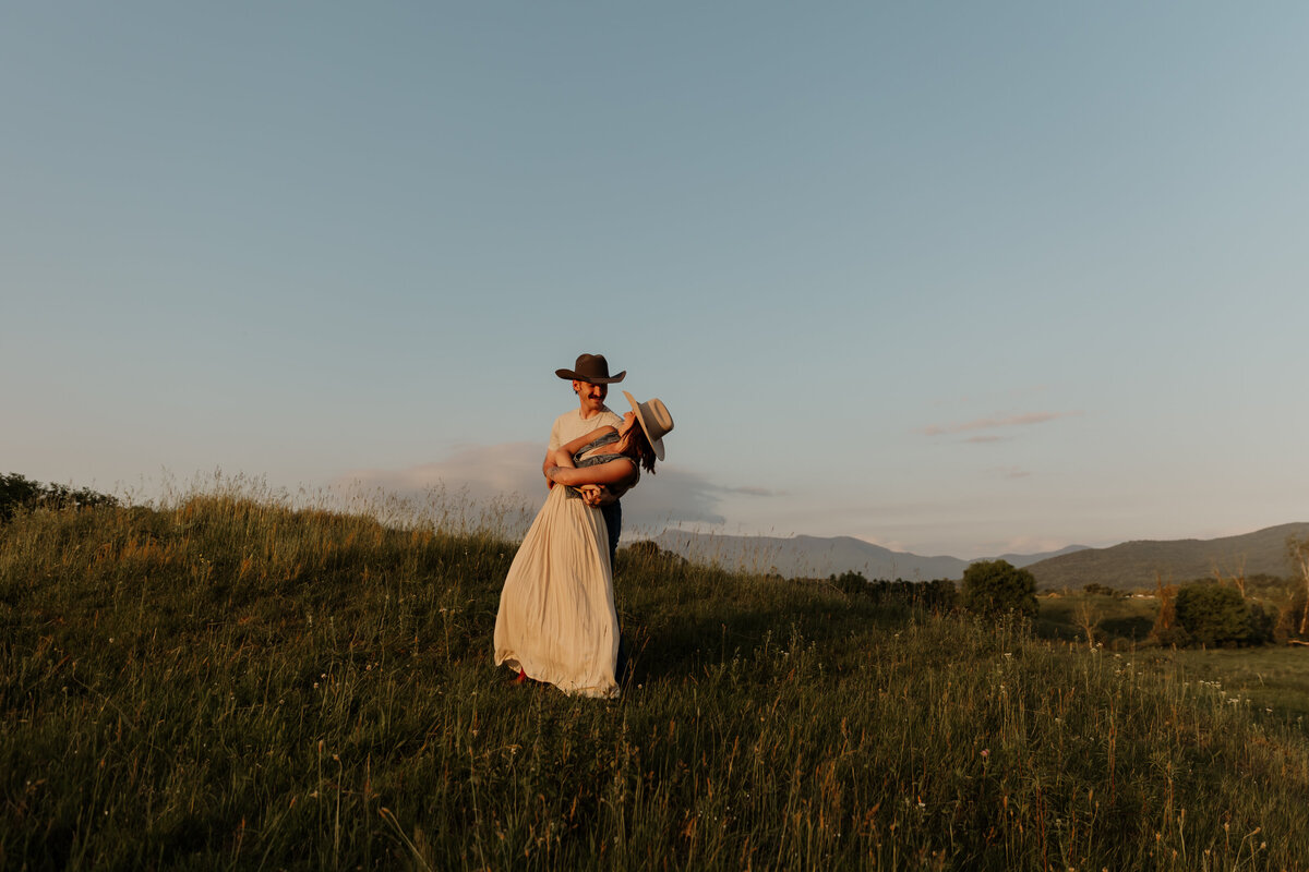 A fine art New England photographer documents an engagement photoshoot as the dances on a hilltop together. They share a laughter while surrounded by the mountains of New England—a loving and timeless scene perfect for nature-loving couples.