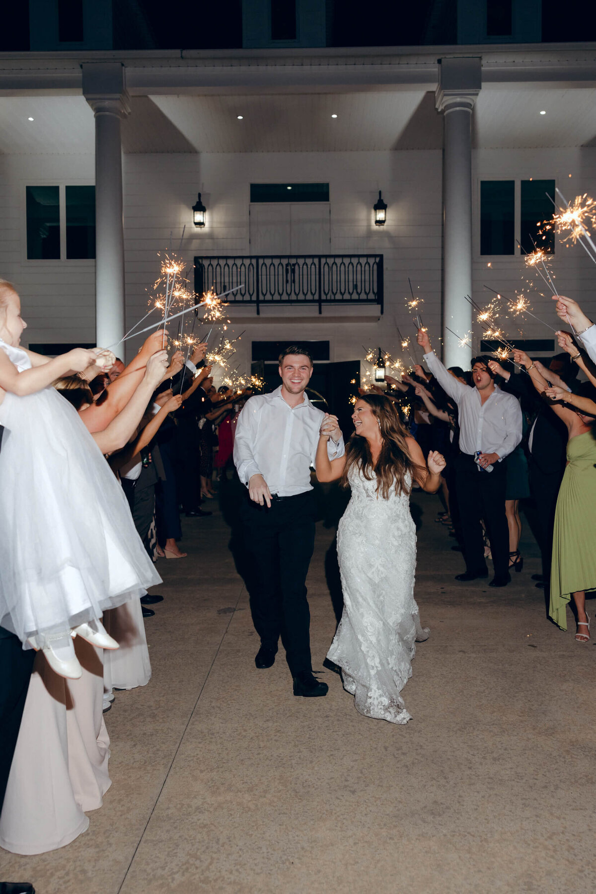 A wedding photo of the bride and groom leaving the wedding reception while guests hold sparklers in the air celebrating
