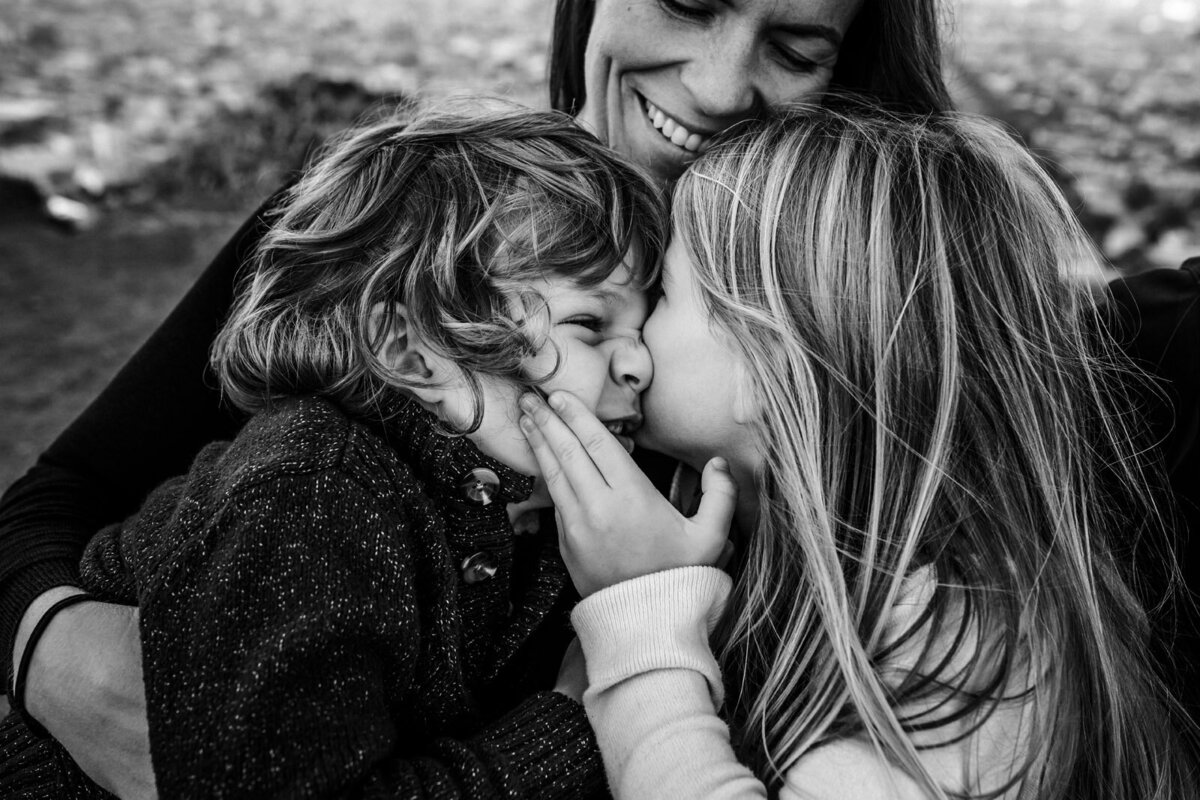 brother and sister squishing their faces close together with mom looking down and smiling