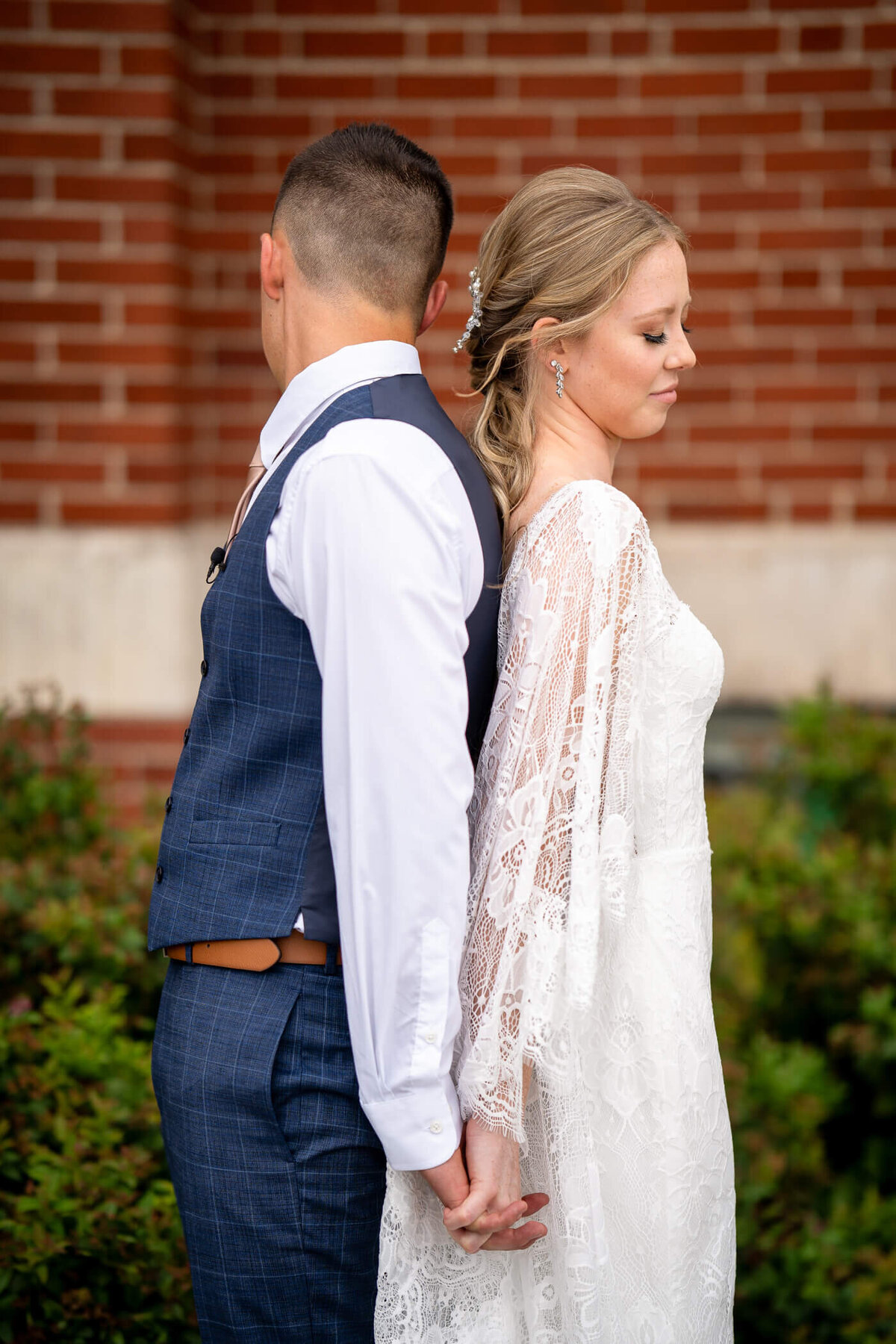 wedding photos of bride and groom stand back to back and hold hands during their first look and vowel reading at their local church.