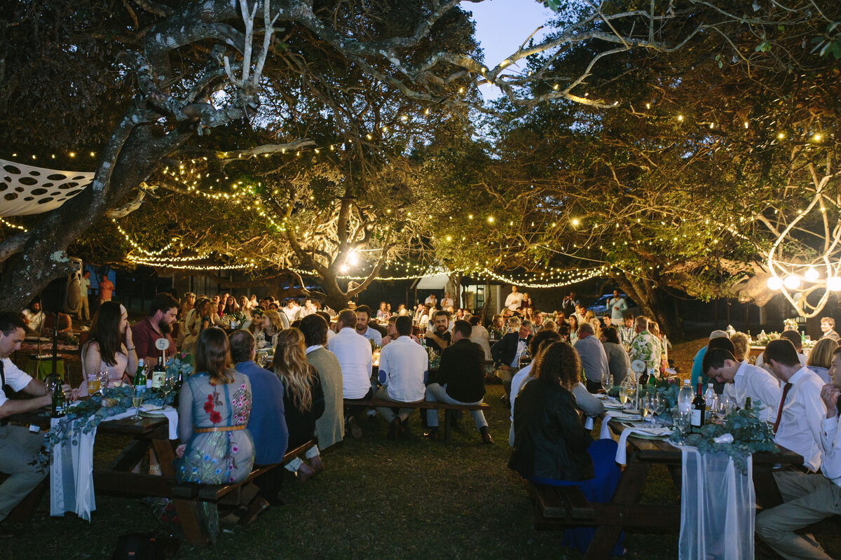 Candid moment at an outdoor wedding reception, surrounded by trees, glowing candles, and hanging lights.