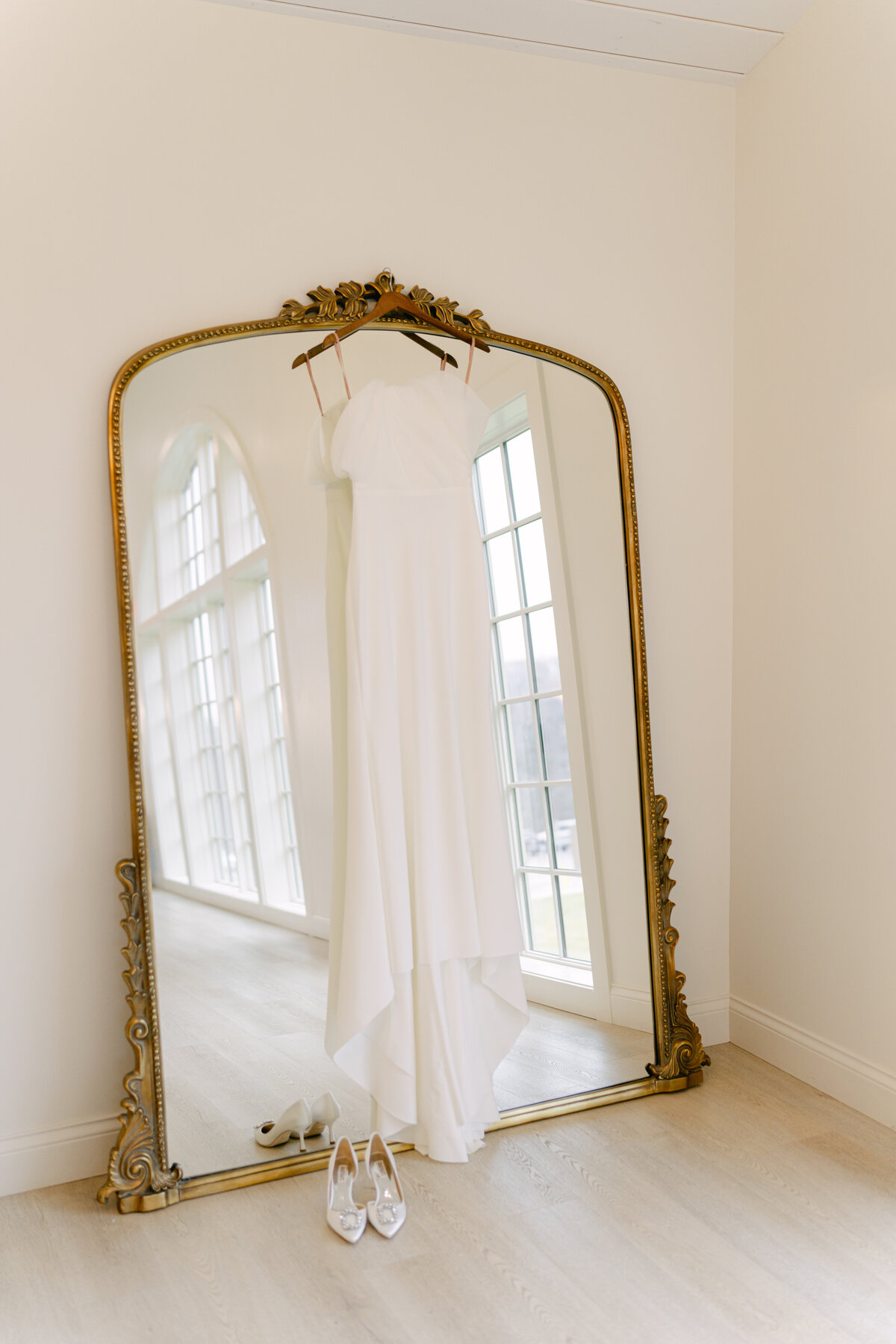  A classic bridal gown hangs on golden mirror at Westwind Hills Venue taken by Lacey Graham a Luxury Wedding Photographer in Illinois