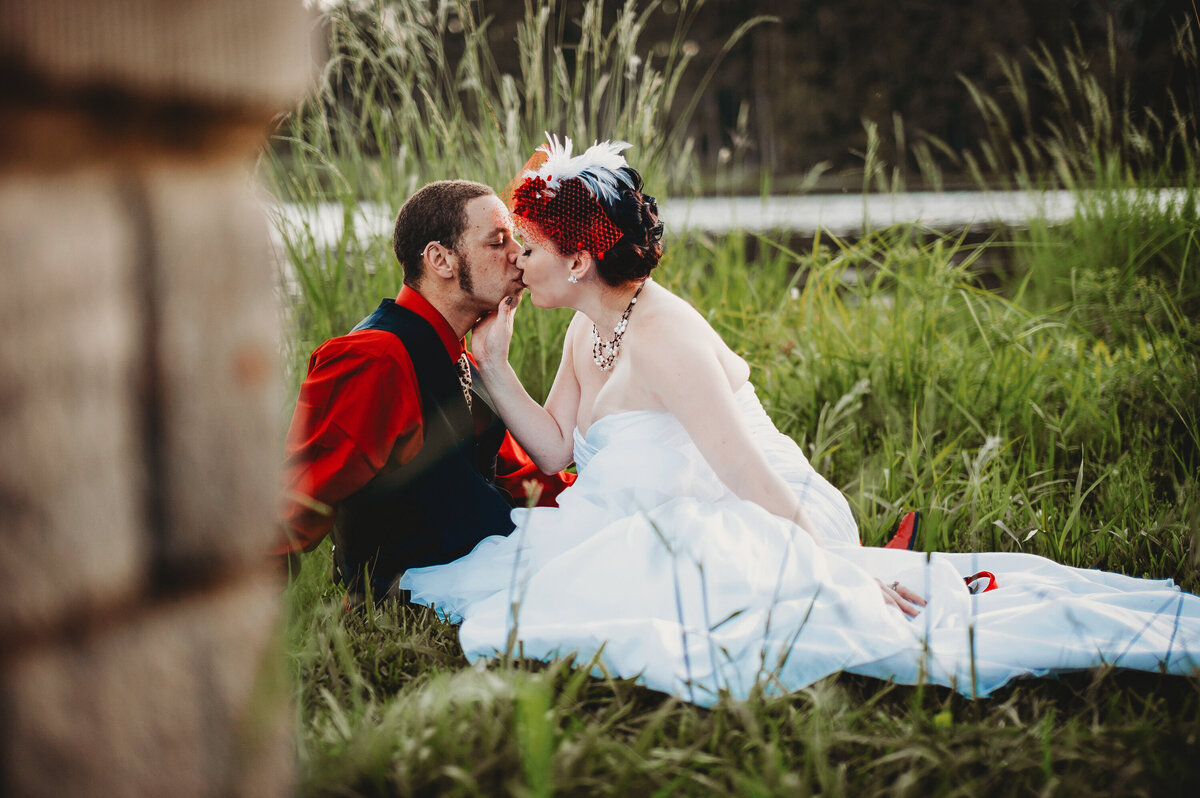Intimate wedding portrait of bride and groom sitting in a grassy field in Orlando sharing a kiss.