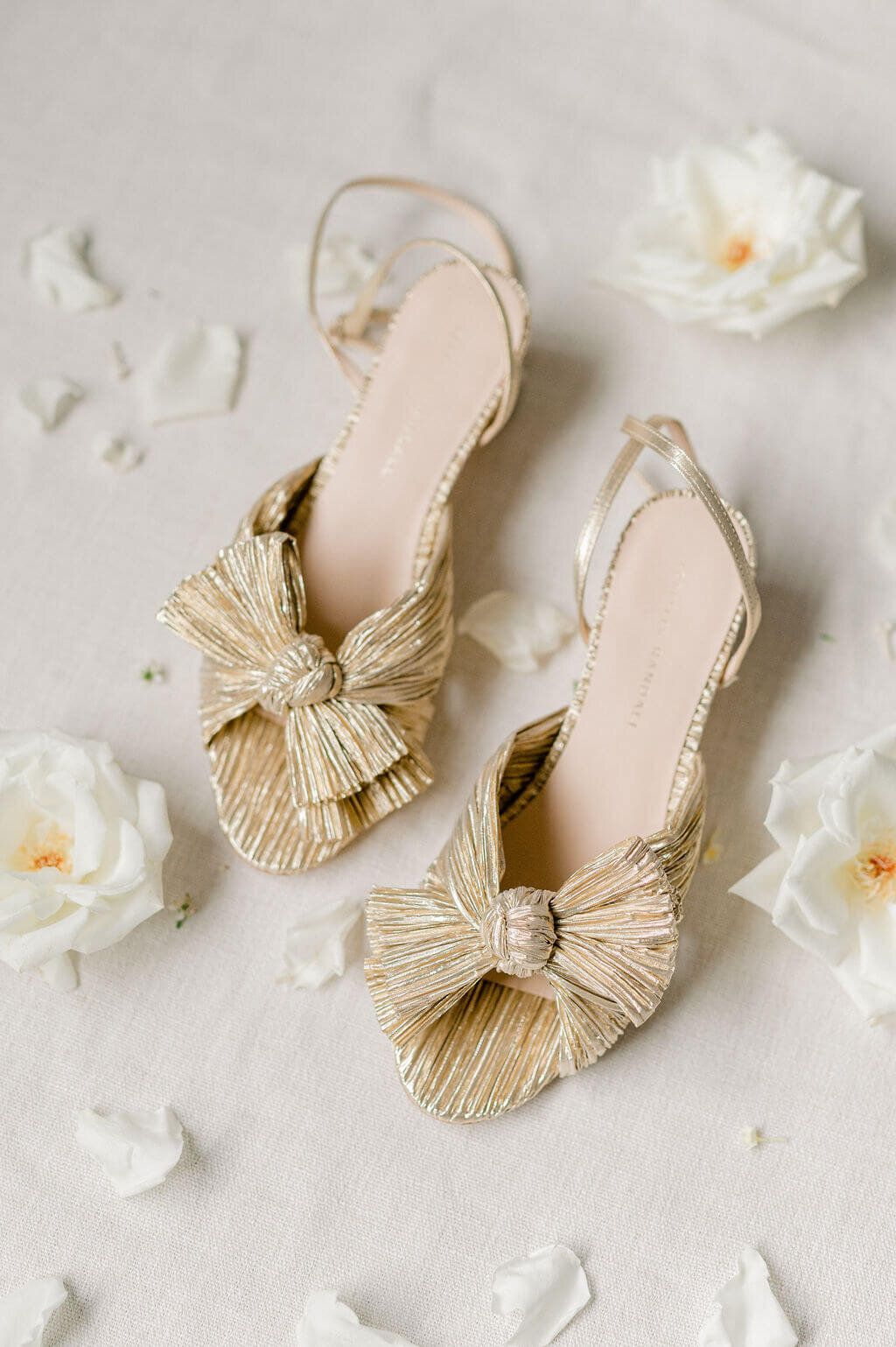Golden Loeffler Randall bridal shoes surrounded by white roses.