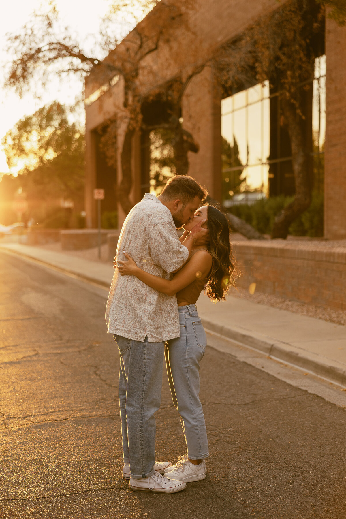 A couple standing in the street kissing at sunset.
