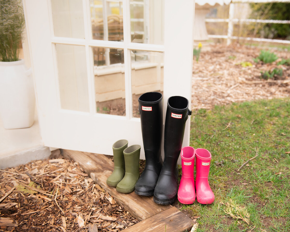 A charming lifestyle detail photo of a set family rain boots outside the floral greenhouse setup during a spring session in Dundas, Ontario at All Who Wander Flower Farm.