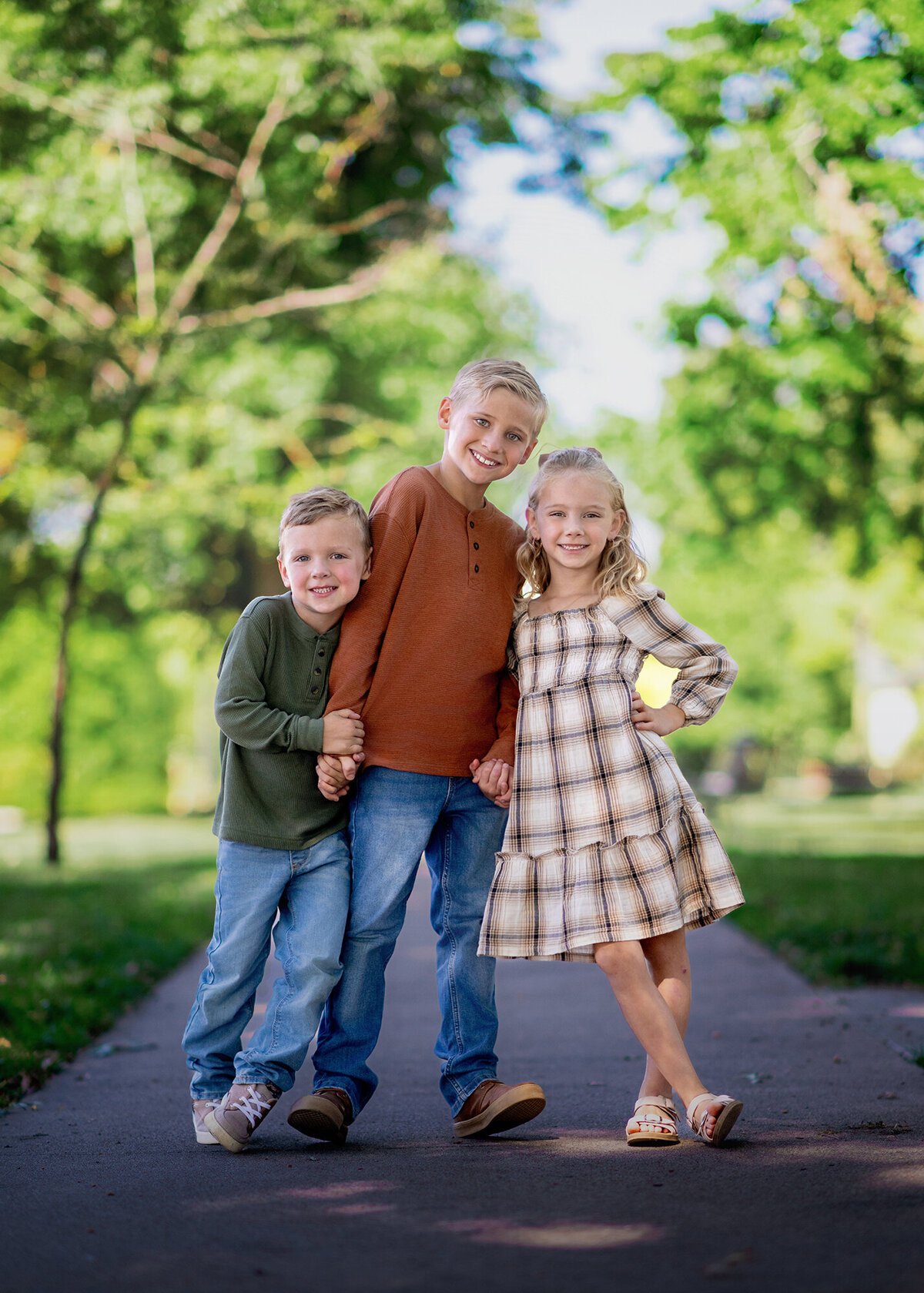 A trio of kids standing close on a path in a scenic outdoor garden with their Iowa Family Photographer