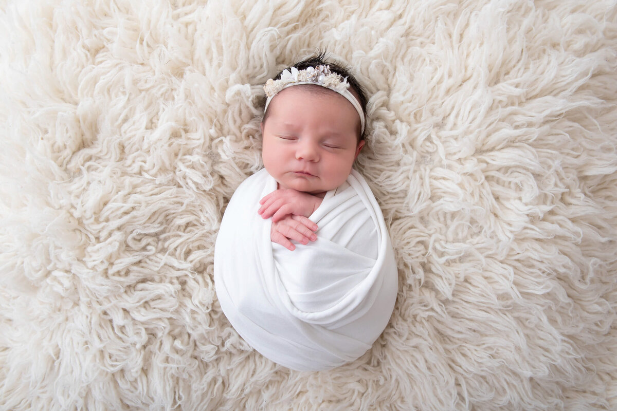 Newborn baby girl wrapped in white with a white headband for her newborn photography session in Burlington, Ontario