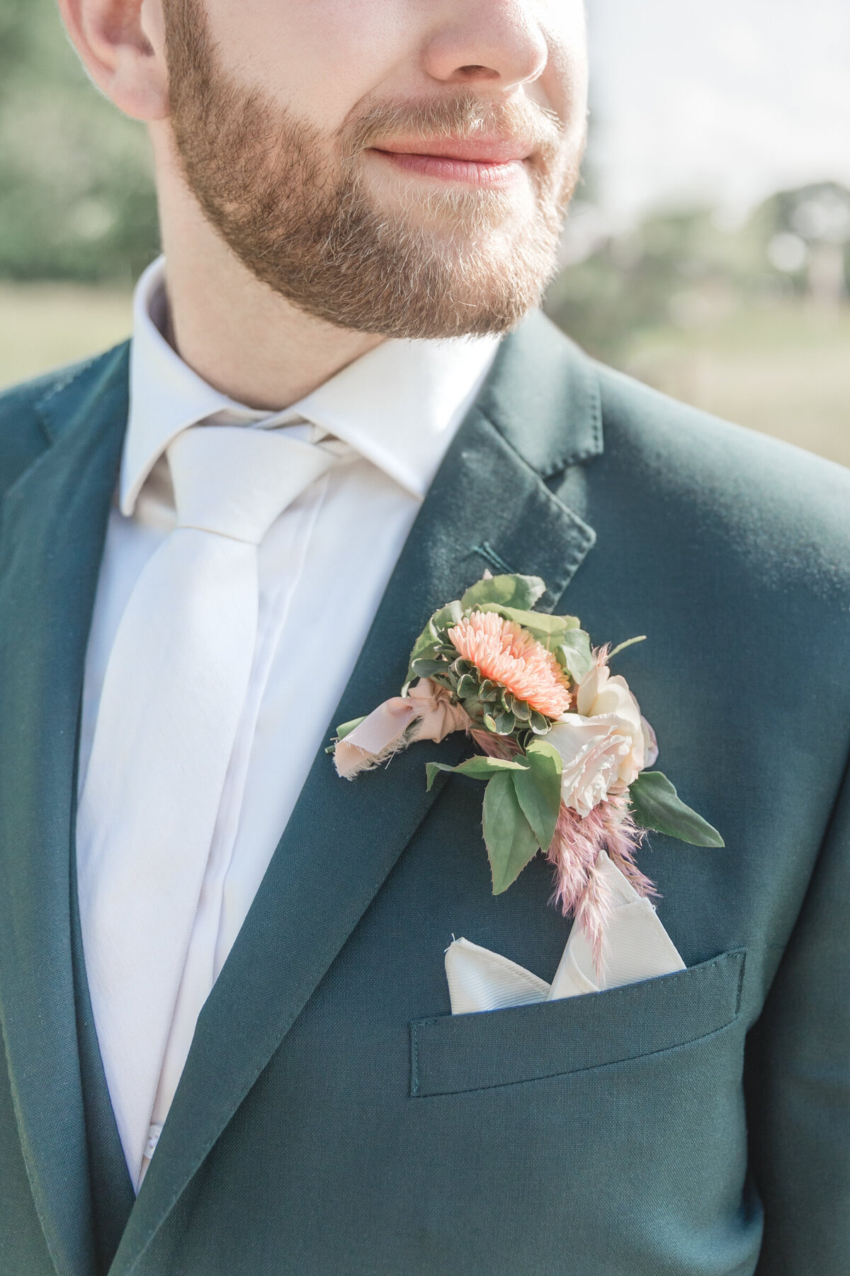 A close up of a peach boutonniere and groom in a dark green suit
