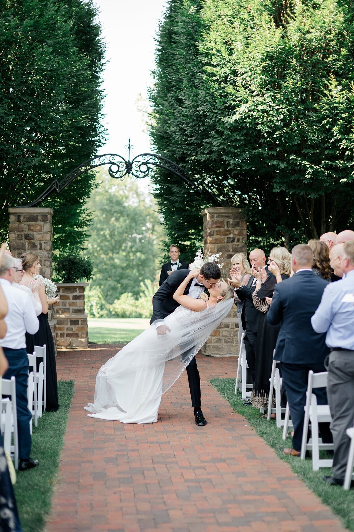 groom dips his bride backwards in the middle of the aisle as they exit their outdoor ceremony