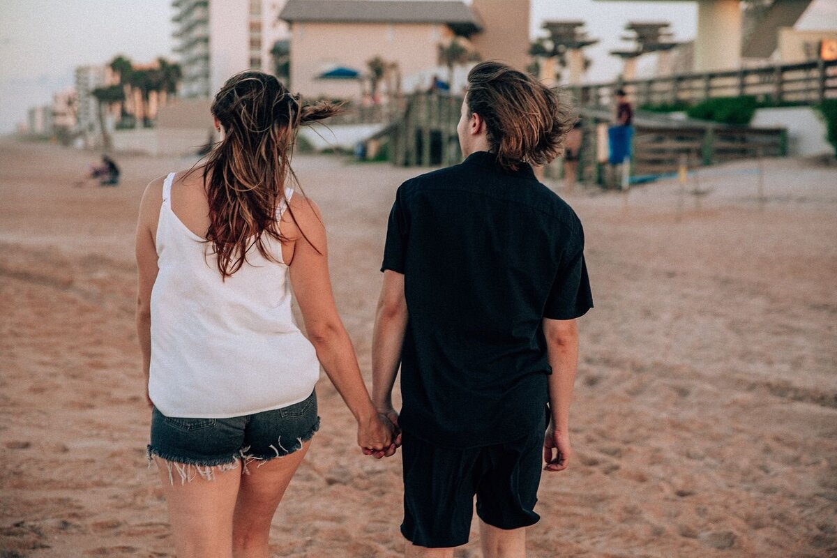 engaged couple walking on ormond beach holding hands