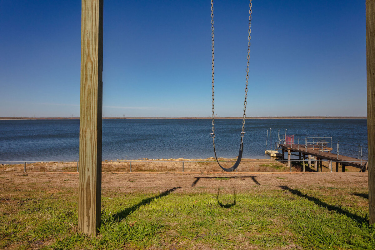 Swing overlooking the lake and dock access at this 2-bedroom, 2-bathroom lakeside vacation rental home for 6 guests on Tradinghouse Lake with privacy access to a fishing dock and boat launch pad, ping pong table, gazebo, free wifi and free parking in Waco, TX.
