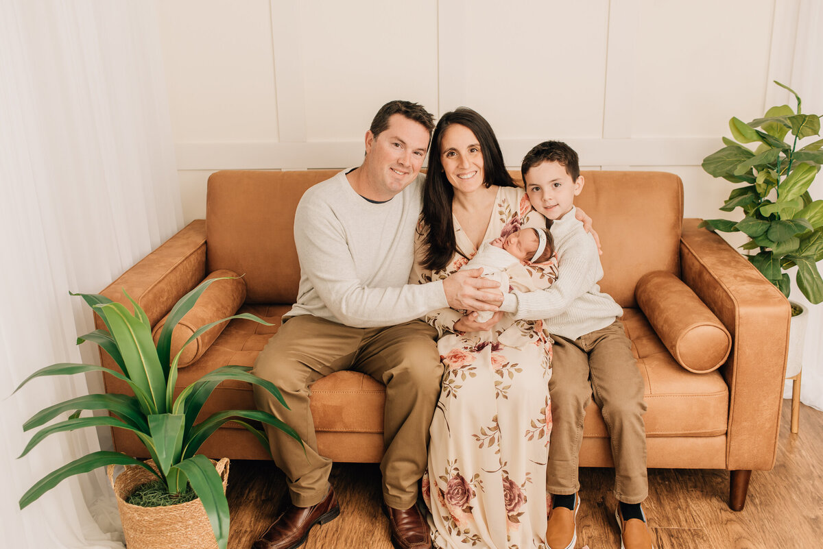 A family of four smiling at the camera at their studio newborn session in Canton, CT.