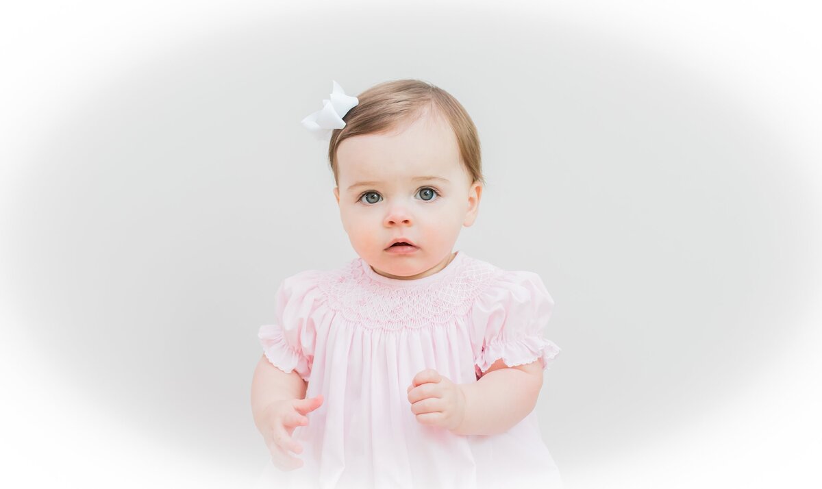 Baby girl in a pink smocked dress with a bow in her hair.